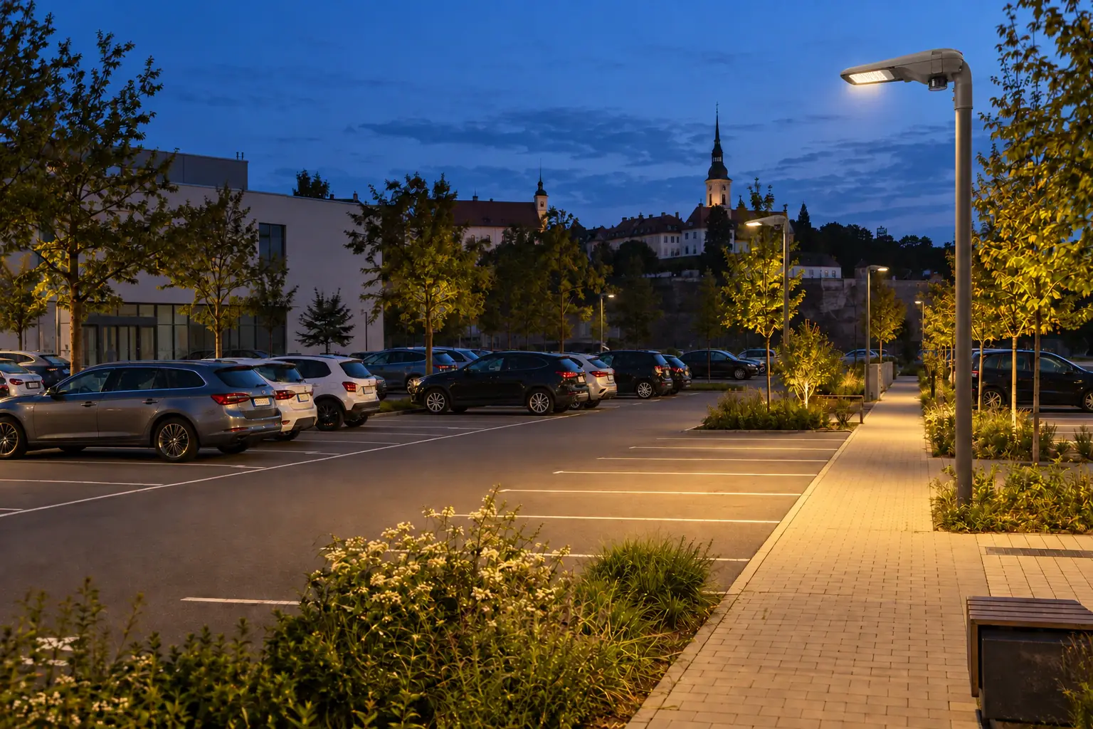 Öffentlicher Parkplatz zur blauen Stunde mit Fahrzeugen und gerichteter Beleuchtung.