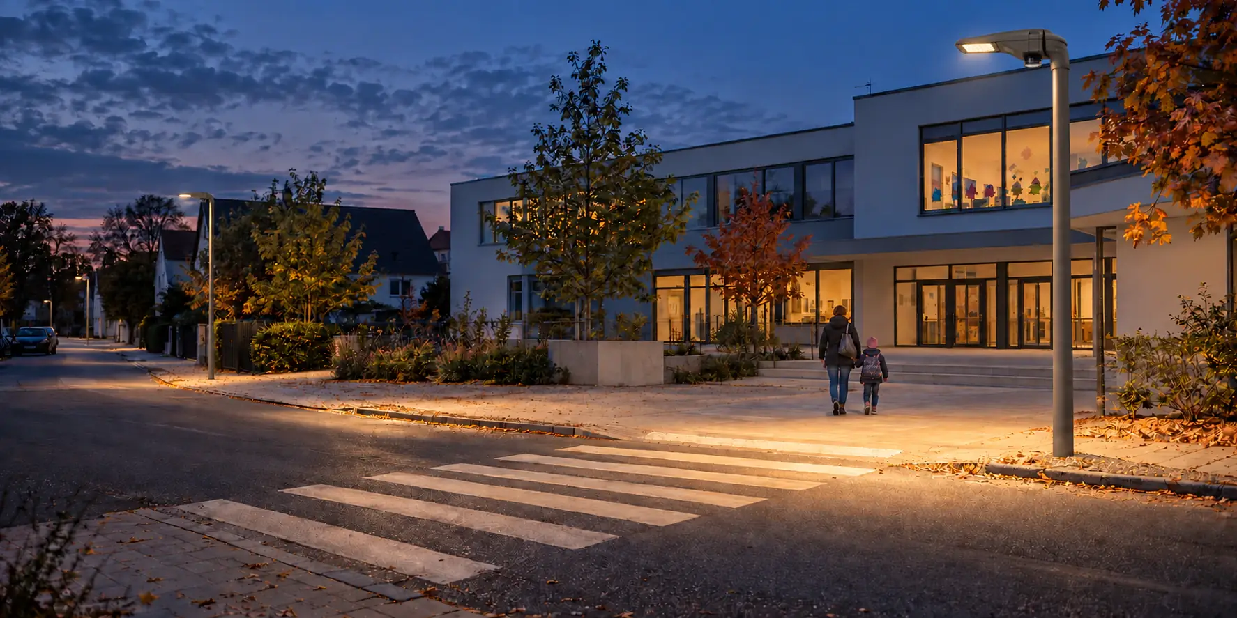 Straße vor einem Schulgebäude in der Dämmerung mit beleuchtetem Übergang.